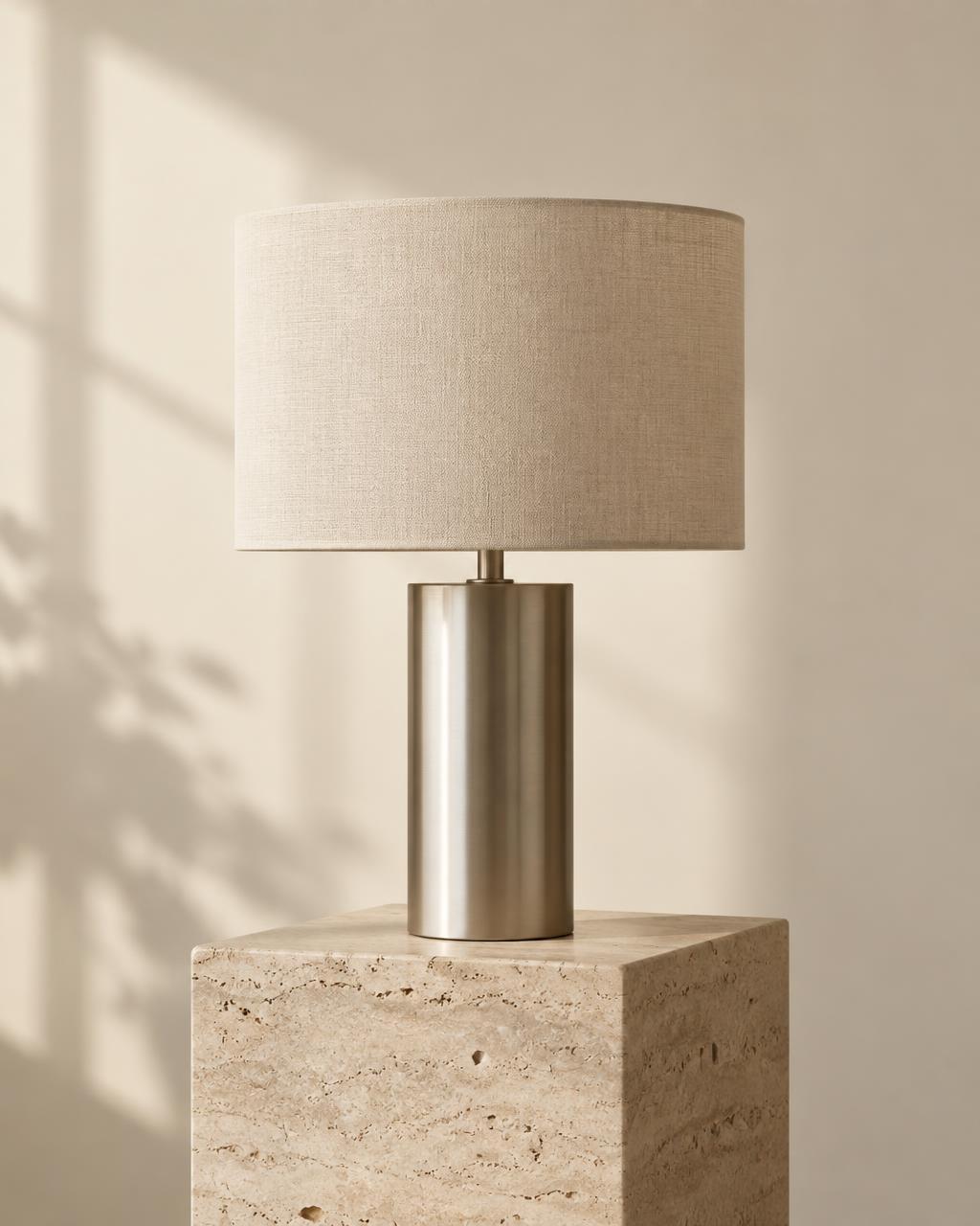Brushed metal table lamp with a linen shade on a travertine plinth